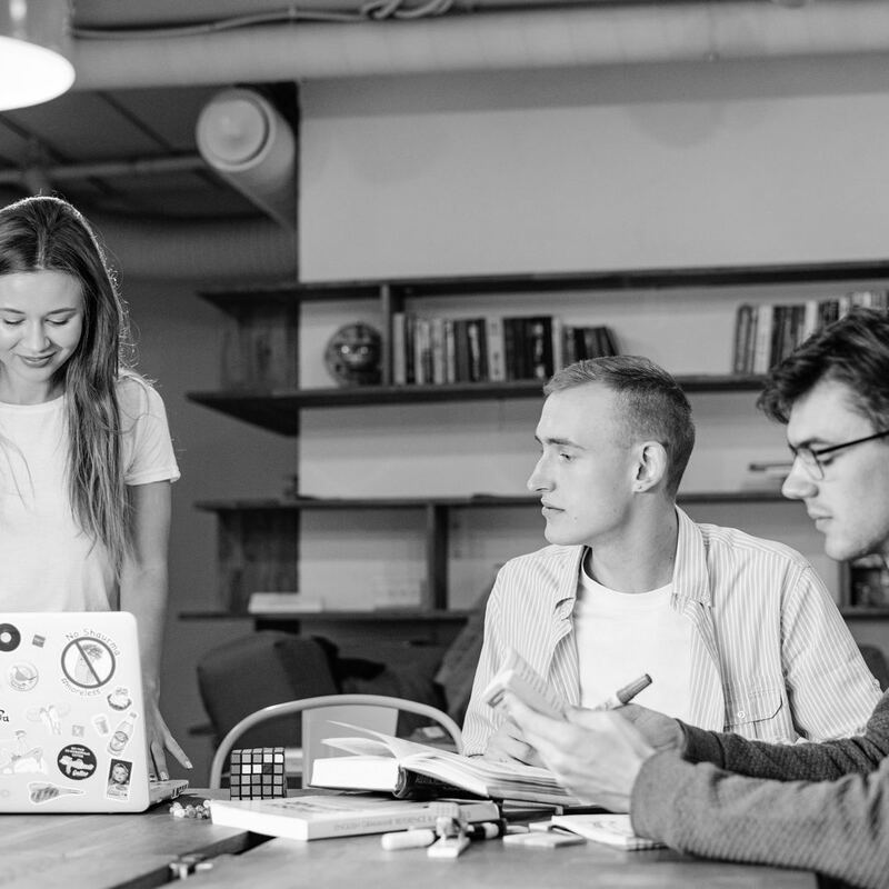 Three young professionals collaborating at a laptop, in black and white